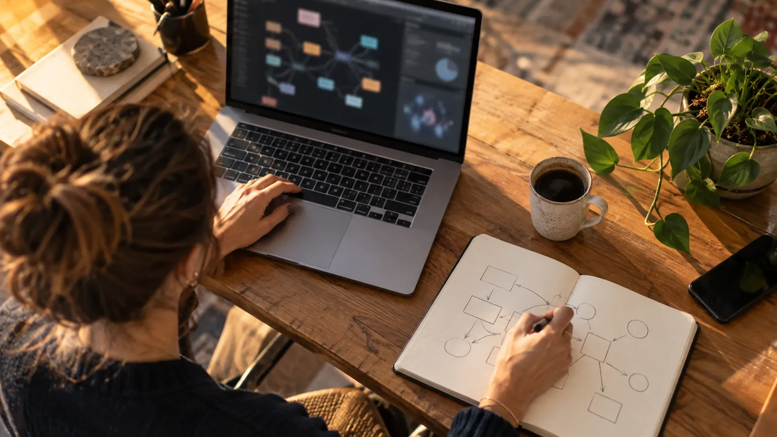 Bureau en bois avec ordinateur, carnet de schémas, café et plante